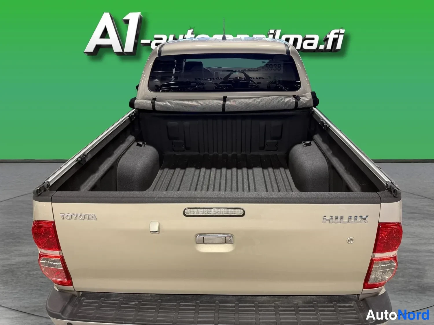 Takaa: Takaaparakuva Toyota Hilux -lava-autosta, jonka pehmeä kansipressu on rullattu kokonaan auki; takakantta avataan, lavassa on muovivuoraus.