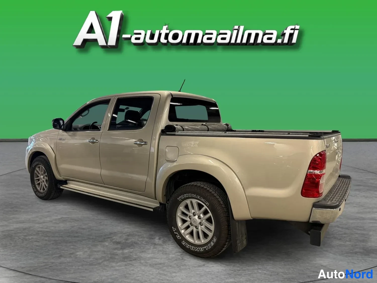 Takaviisto: Beige Toyota Hilux Double Cab -malli kulmassa kuvattuna perä vasemmalle, takaosan ja oikean sivun näkyessä.