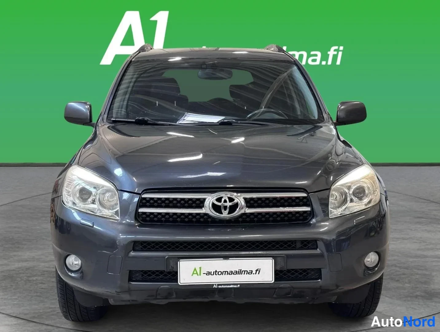 Edestä: Tummanharmaan Toyota RAV4 -maasturin suora etunäkymä, josta erottuvat Toyota-merkillinen etusäleikkö ja molemmat ajovalot.