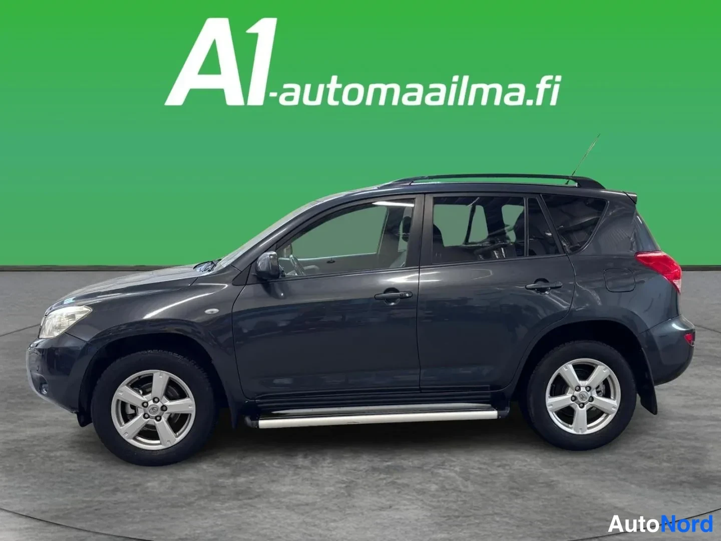 Etuviisto, nokka vasemmalle: Tummanharmaa Toyota RAV4 kolmivaihekulmassa edestä vasemmalta studio­taustaa vasten; näkyvissä kylki, etunoja, kattokaiteet ja sivulaitelahjat.