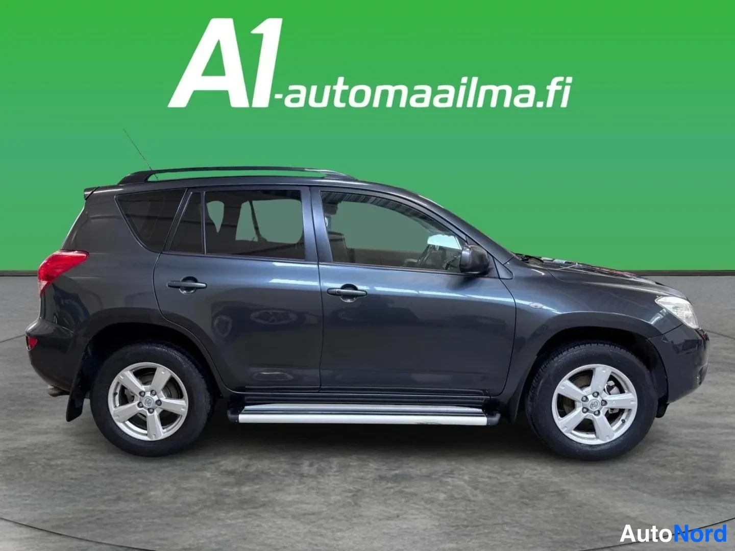 Etuviisto, nokka oikealle: Tummanharmaa Toyota RAV4 kolmivaihekulmassa edestä oikealta studio­taustaa vasten; näkyvissä kylki, etunoja, kattokaiteet ja sivulaitelahjat.
