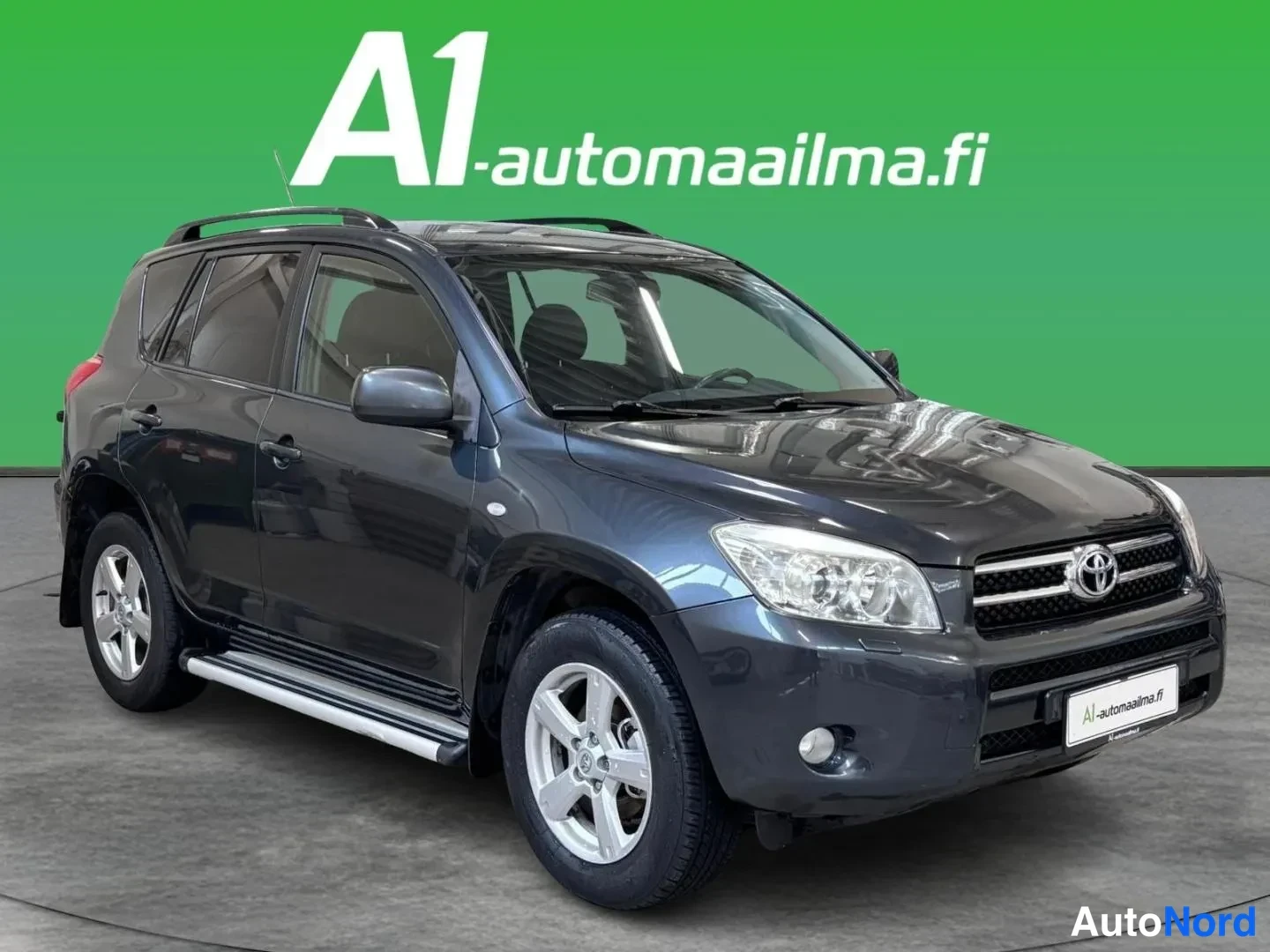 Etuviisto, nokka oikealle: Tummanharmaa Toyota RAV4 kuvattuna etuokoläkuvakulmasta, jossa auton keula on kuvan oikeassa reunassa ja vasen sivu näkyy keskeisesti.