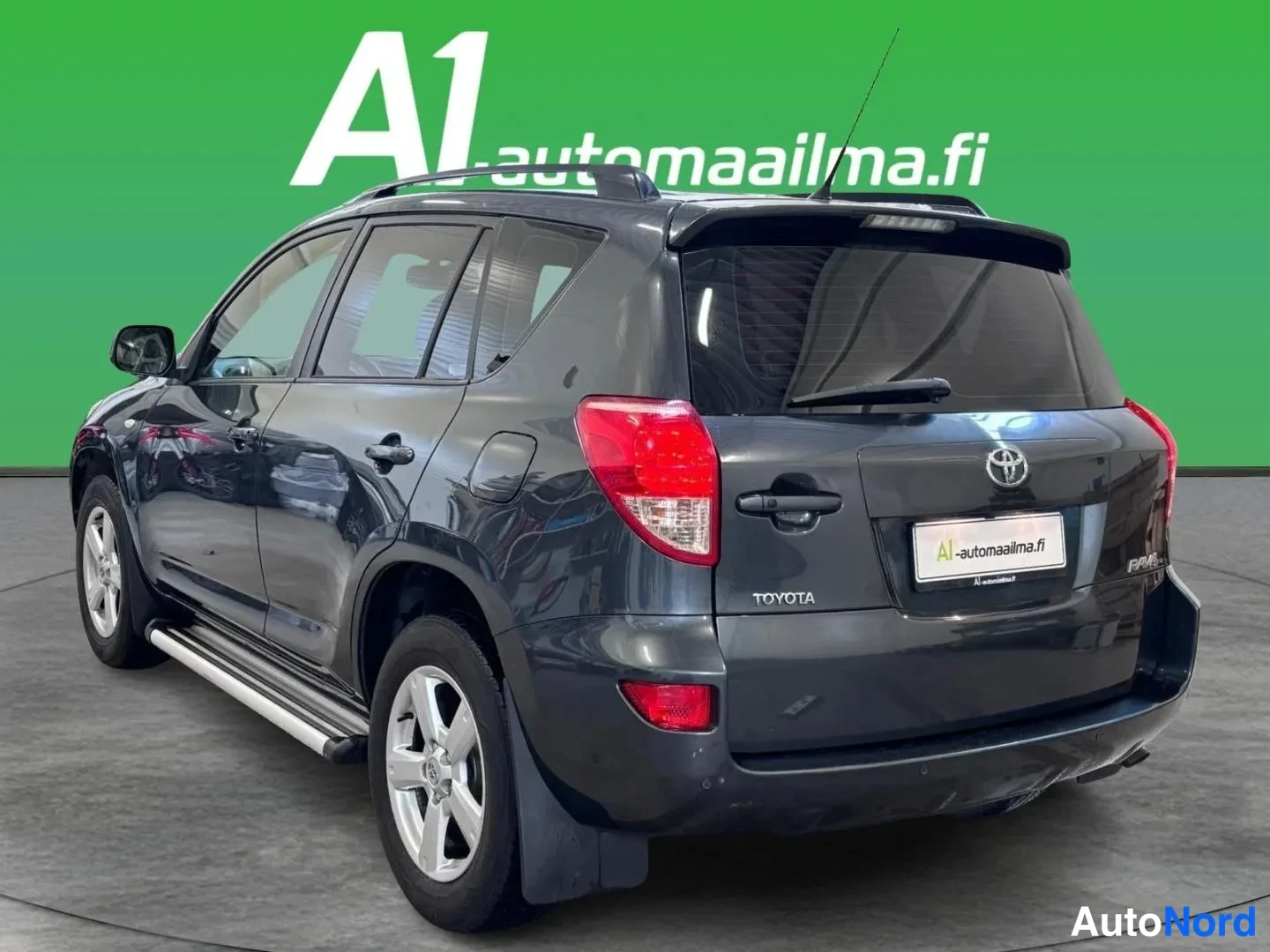 Takaviisto: Tummanharmaan Toyota RAV4 -maasturin takanolikuvakulma, josta näkyvät punaiset takavalot, takaluukun Toyota-merkki ja auton vasen sivu.