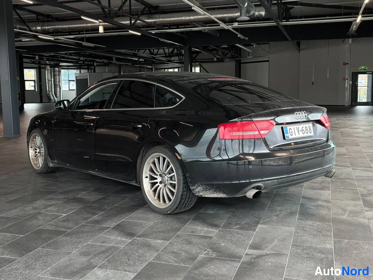 Takaviisto: Mustan Audi Sportbackin takakulma nähtynä oikealta takaa autosalissa.