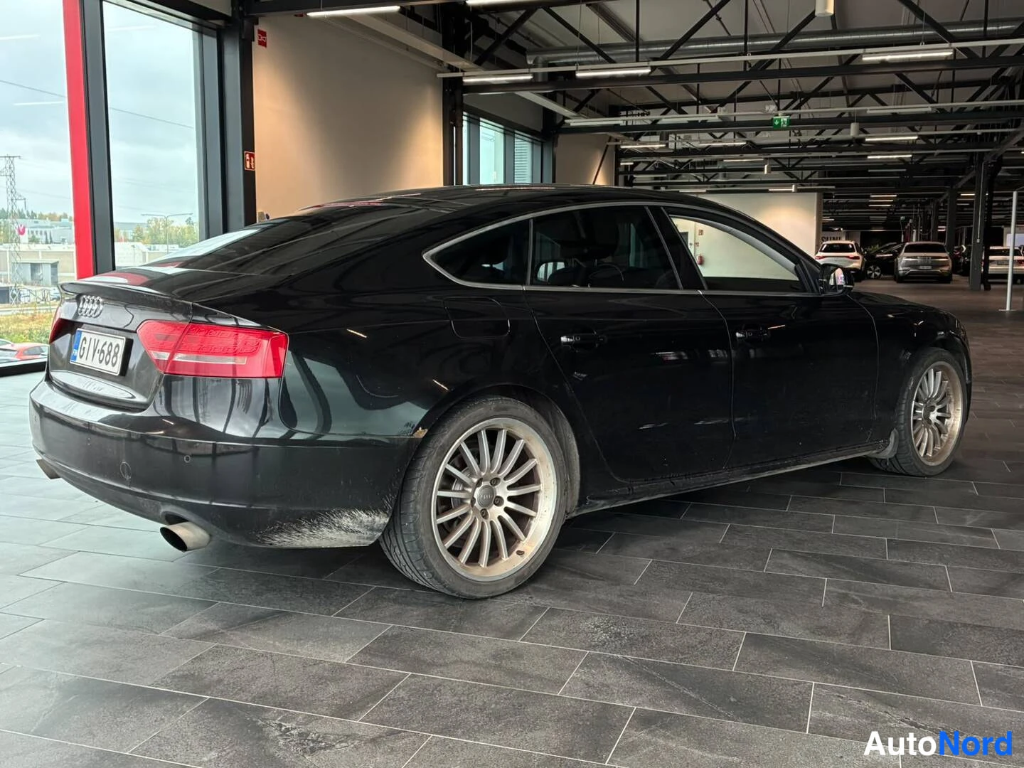 Takaviisto: Mustan Audi Sportbackin takakulma nähtynä vasemmalta takaa autosalissa.