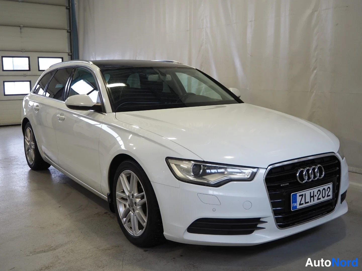 Etuviisto, nokka oikealle: Valkoinen Audi A6 Avant farmari kolmivartalo-etakulmasta sisätilassa, rekisteritunnus.