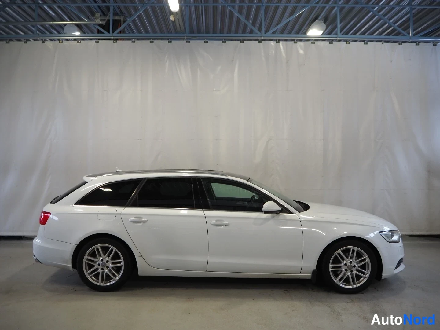 Sivulta: Valkoisen Audi A6 Avant farmarin sivuprofiili sisätilassa.