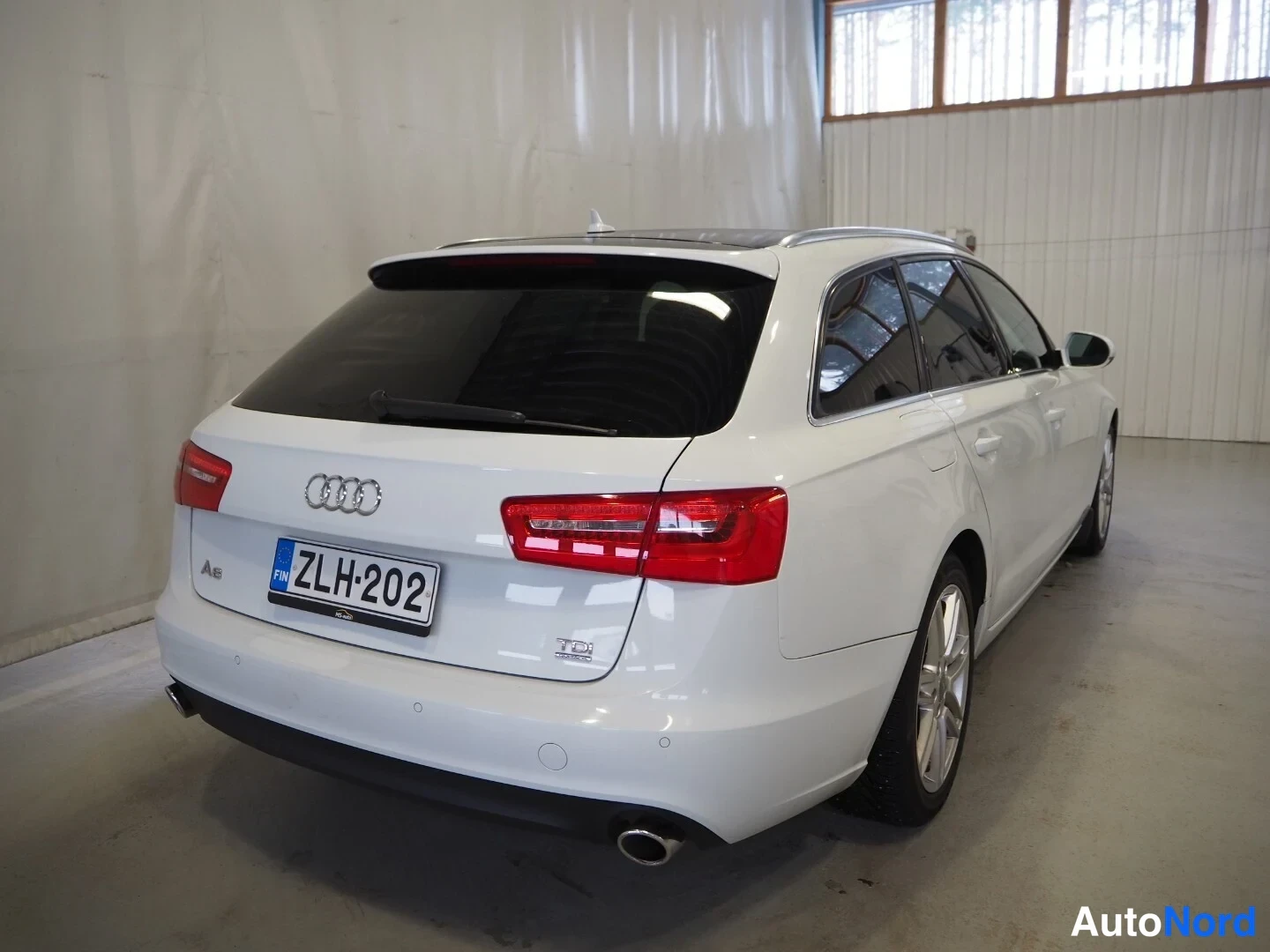 Takaviisto: Valkoisen Audi A6 Avantin takaosakulmakuva sisätilassa, rekisteritunnus.