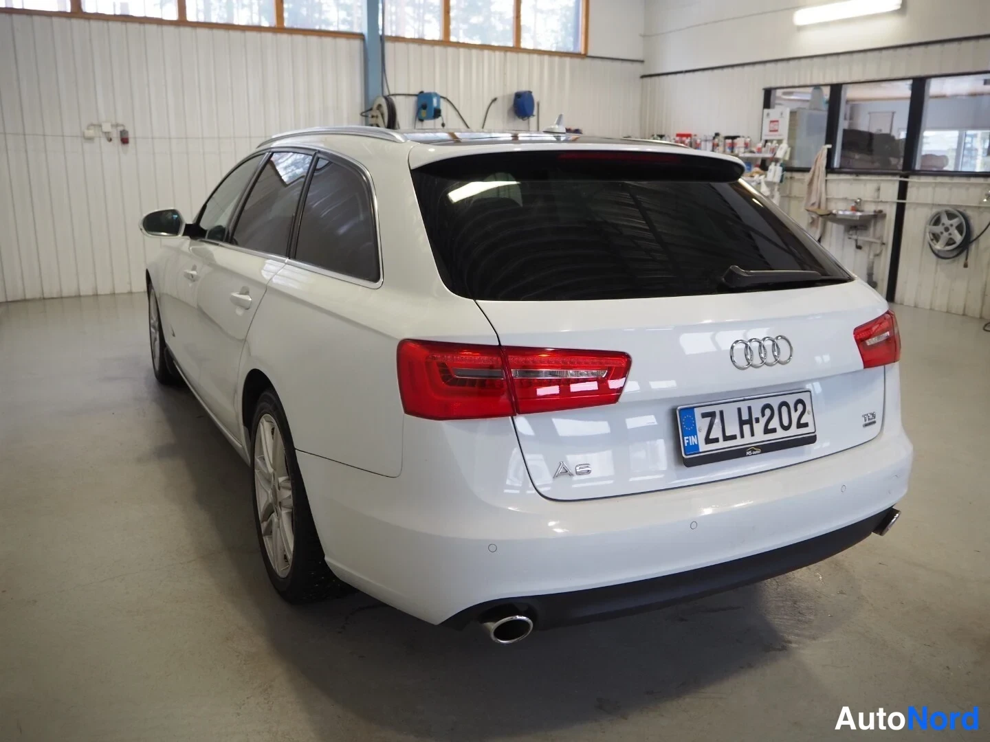 Takaviisto: Valkoisen Audi A6 Avantin takaosakulmakuva korjaamotilassa, rekisteritunnus.