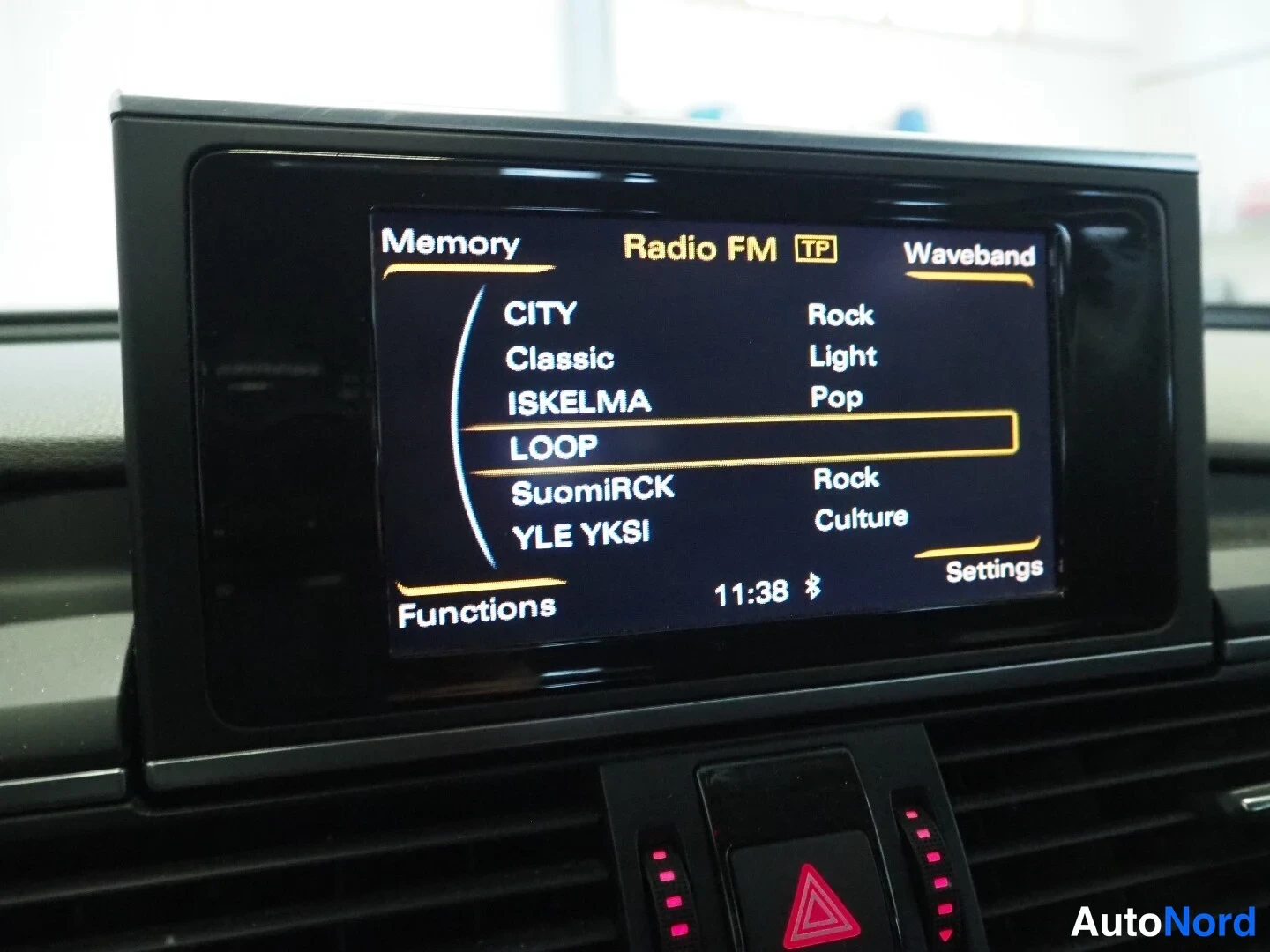Muu: Kojelaudan infotainment-näyttö, jossa radiokanavavalikko (Radio FM TP) ja kellonaika 11:38.