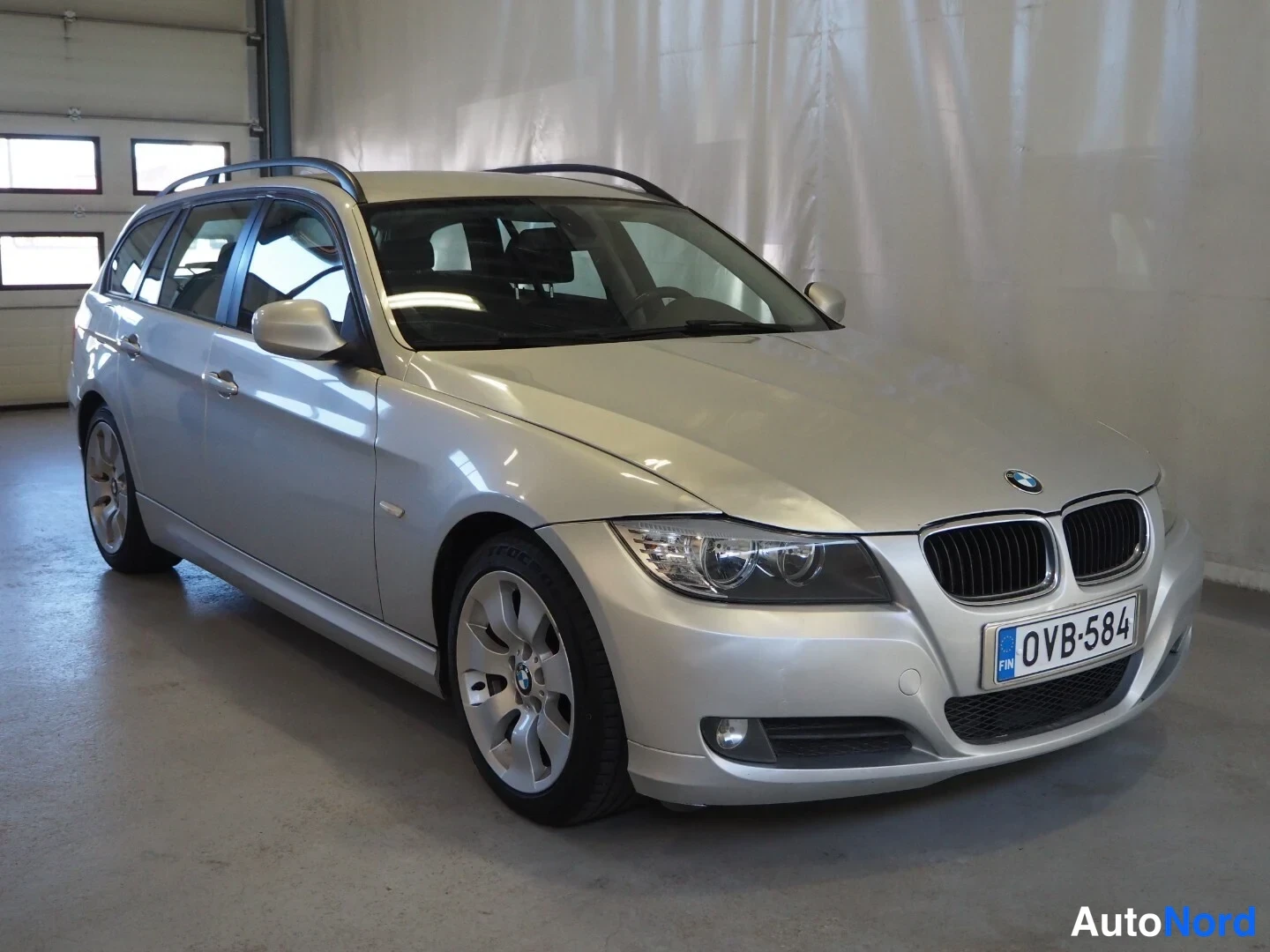 Etuviisto, nokka oikealle: BMW 318d Touring -farmari, etukulmasta oikealta, hopeinen, rekisteritunnus.