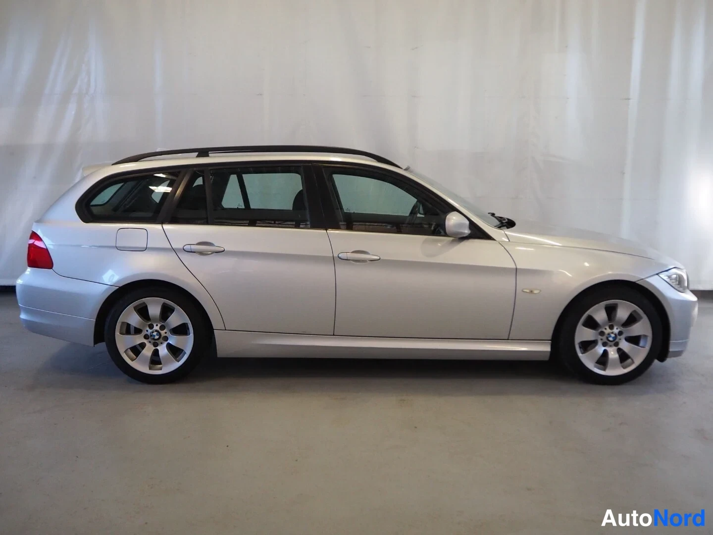 Sivulta: BMW 318d Touring -farmari, sivukuva vasemmalta, hopeinen, kattotangot ja alumiinivanteet.