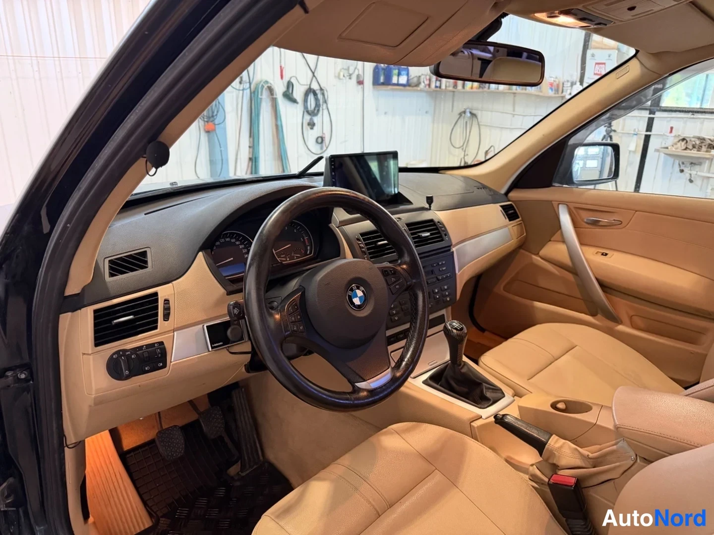 Muu: BMW X3:n kojelauta ja ohjaamotila kuljettajan puolelta: BMW-ohjauspyörä, analogiset mittarit, tumma kojelauta beigellä sisätilalla, vaihdekeksi ja koroke, displ