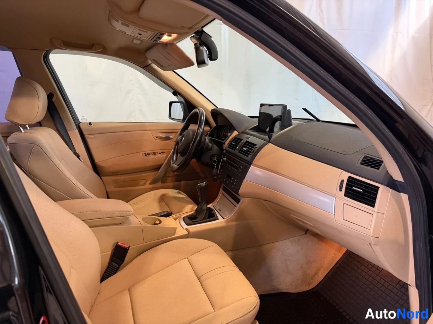 Muu: BMW X3:n matkustamon sisäkuva kyydistä katsottuna: beigeä nahkaa penkeissä ja ovineloissa, tumma kojelauta ja display, vaihdekeksi ja koroke, oviverhoilu ja tav