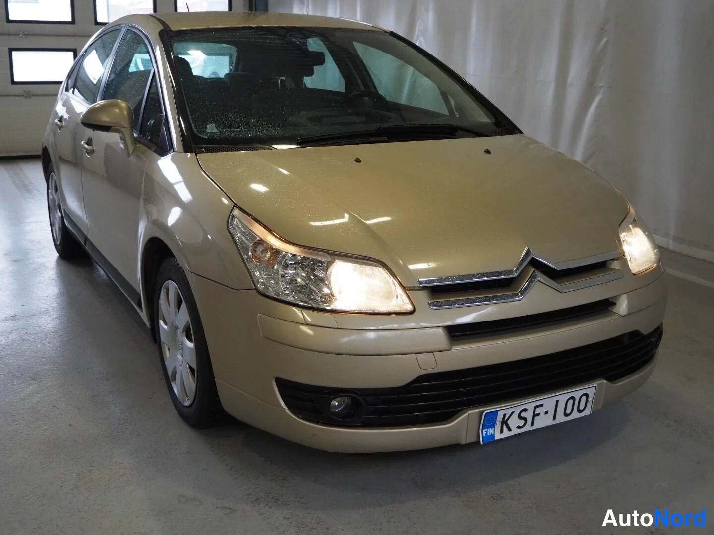 Etuviisto, nokka oikealle: Kulta­vaalean Citroën C4 -henkilöautin etukolmasel näkymä; etumoitto ja kylki näkyvät sisätiloissa.