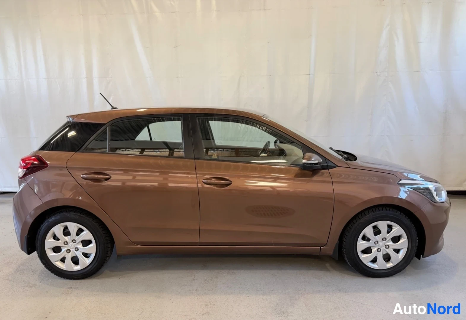 Sivulta: Ruskea Hyundai i20 -henkilöauto sivulta sisätiloissa, oikeanpuoleinen kylki ja neljä ovea näkyvissä.