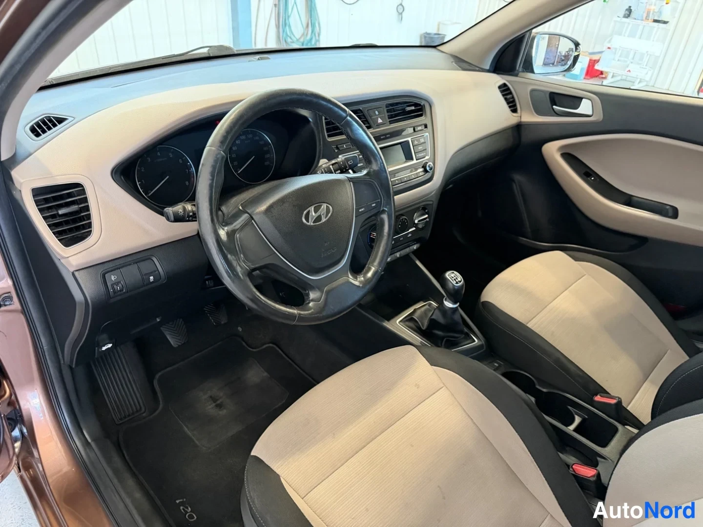 Sivulta: Hyundai i20:n ohjaamo etuovesta kuvattuna: Hyundai-ohjauspyörä, mittaristo, manuaalivaihteisto ja radioyksikkö.