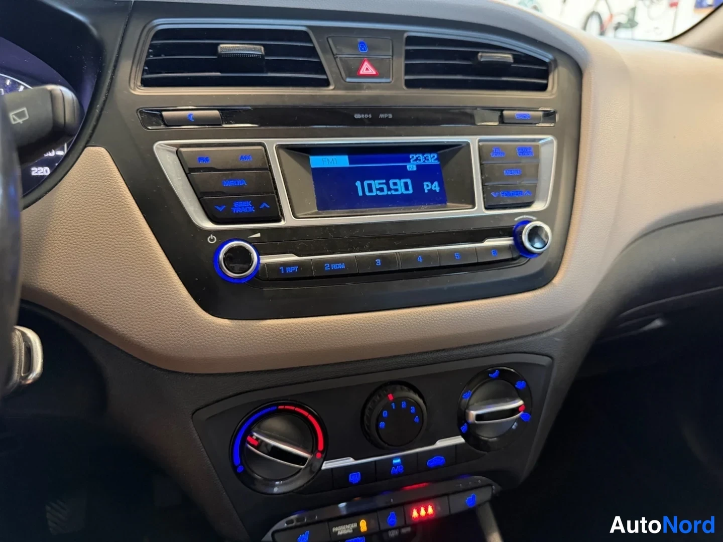 Muu: Kojelaudan keskusyksikkö: radio näyttää kanavan 105.90 ja kellon 23:32, manuaaliset ilmastointisäätimet ja jarrunappi näkyvät.