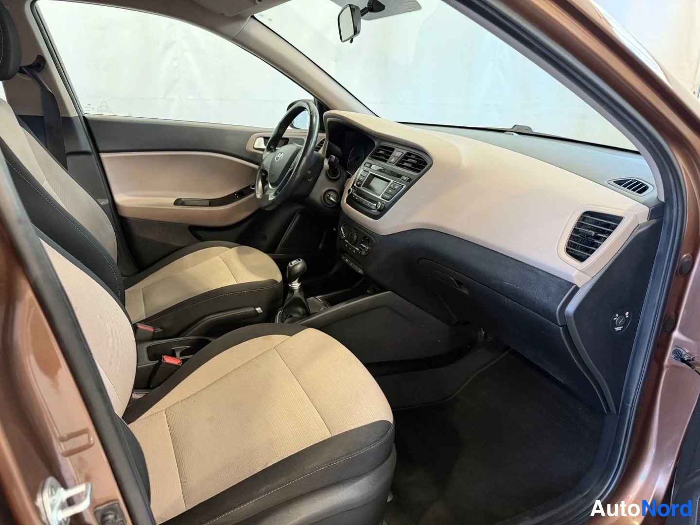 Muu: Hyundai i20:n etusisätila vasemmalta ovelta kuvattuna, beige-mustat istuimet ja kojelauta.