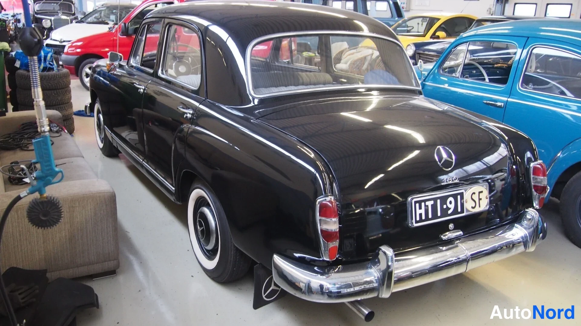 Takaviisto: Mustan Mercedes-Benz 180 -henkilöauton takakolmannes autohallissa, rekisterikilpi.