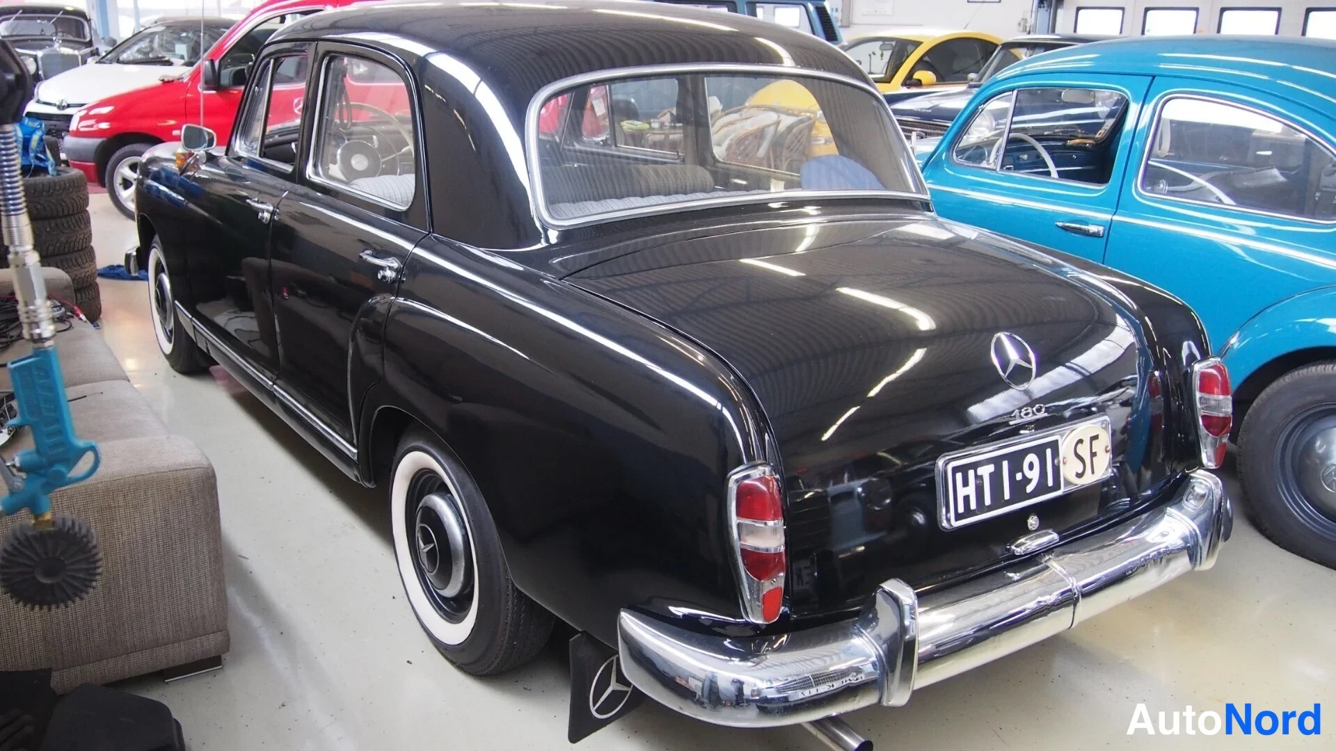 Takaviisto: Musta Mercedes-Benz 180 takaa vasemmalta kuvattuna, kromipuskurit ja rekisterikilpi näkyvät.