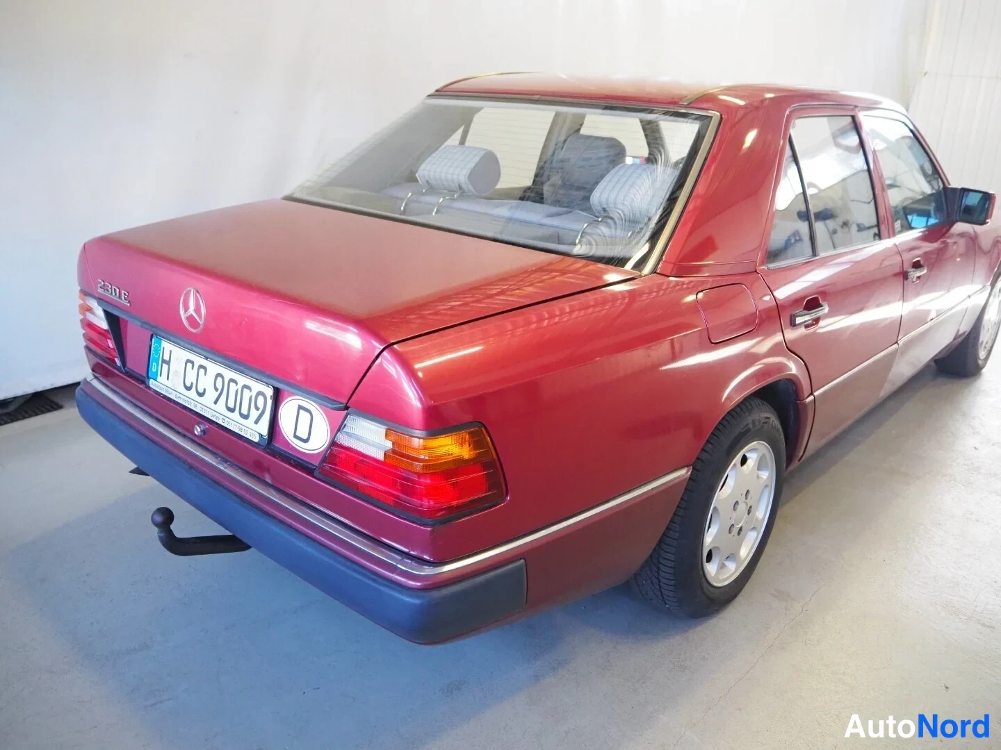 Takaviisto: Punaisen Mercedes-Benzin takakolmannes: takavalojen ja merkin välissä kyltti 'H CC 9009' ja '230E'-merkintä, peräosassa vetokoukku.