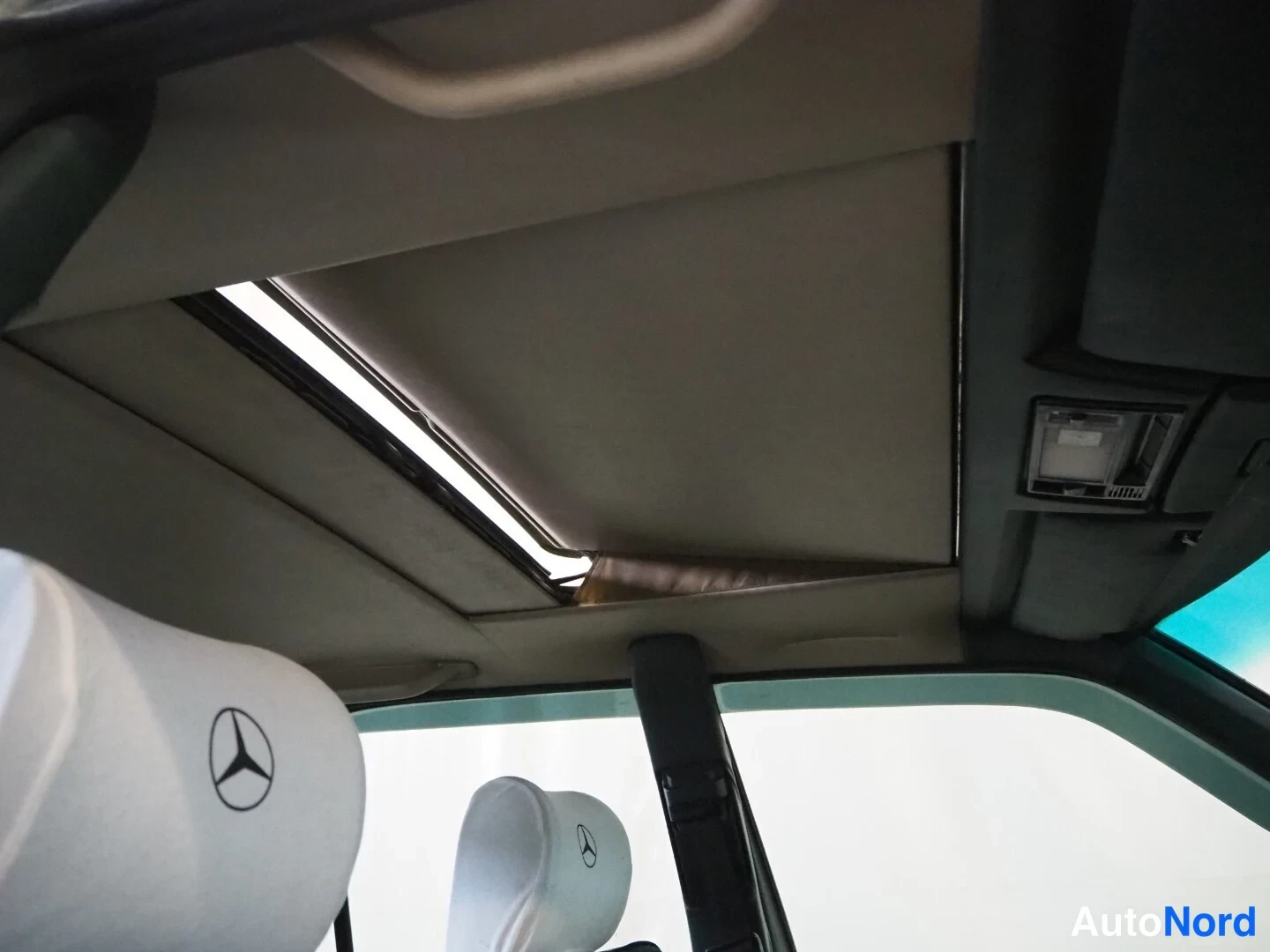 Sivulta: Autojen sisätilat: avattava kattoikkuna (sunroof), vaalea kattoa sementti ja Mercedes-emblemät pääntuessa.