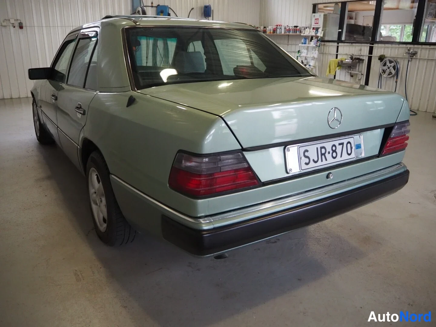Takaviisto: Mercedes-Benz W124-sedanin takakulma koritilassa, vihreä kori, rekisterikilpi näkyvissä.