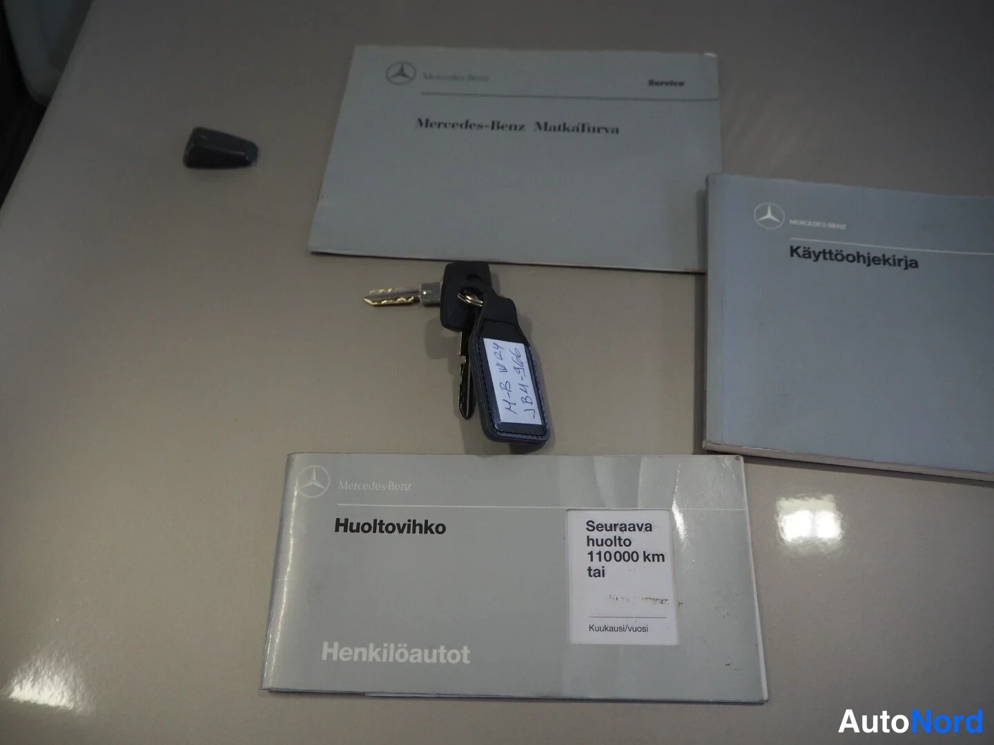 Muu: Pöydällä avaimet ja Mercedes-Benzin huolto- ja käyttöohjekirjat, huoltovihko päällimmäisenä.