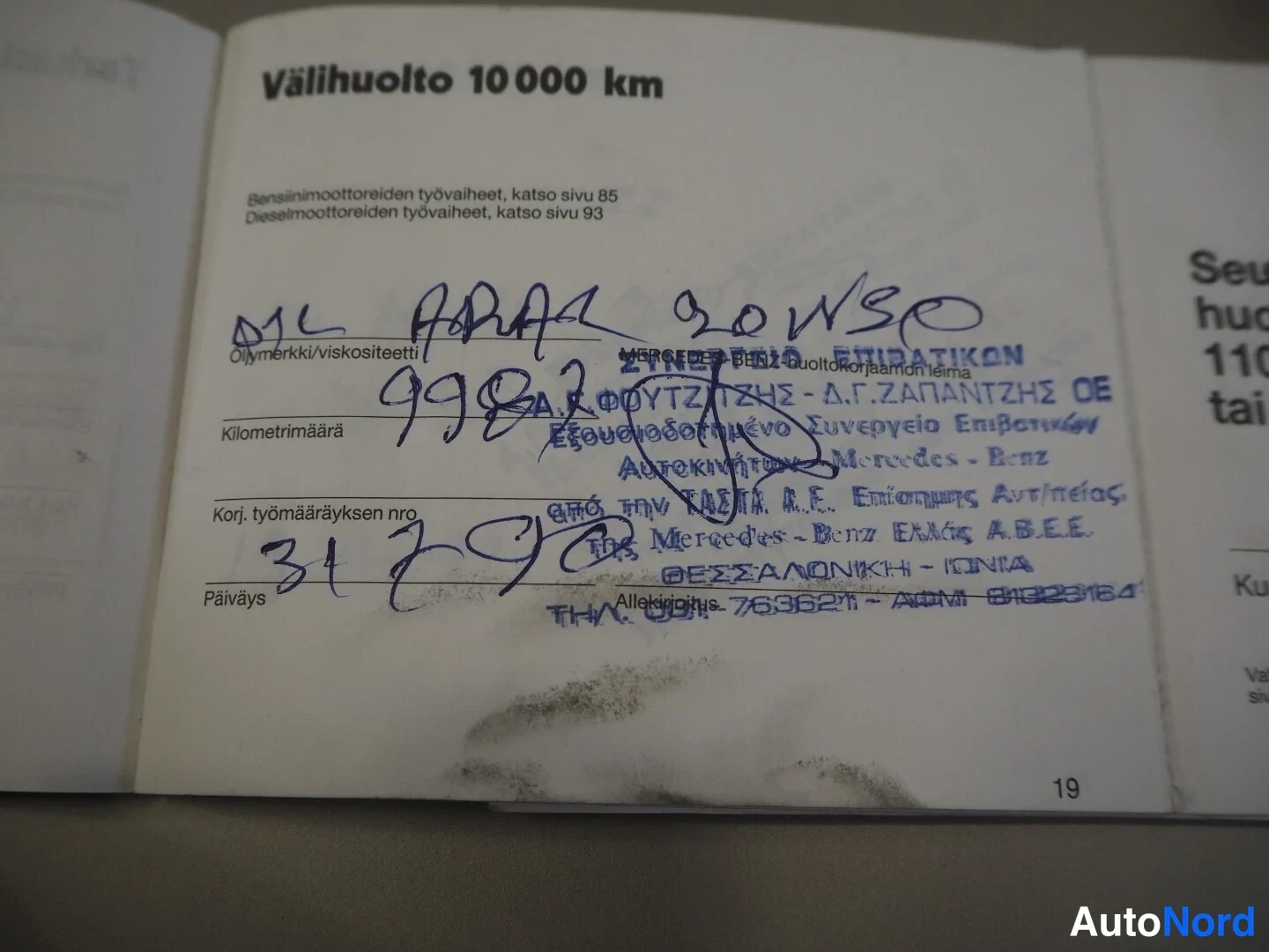 Yksityiskohta: Huoltokirjan sivu 19: Välihuolto 10 000 km, käsiala ja sininen leima, alaosassa tahra.