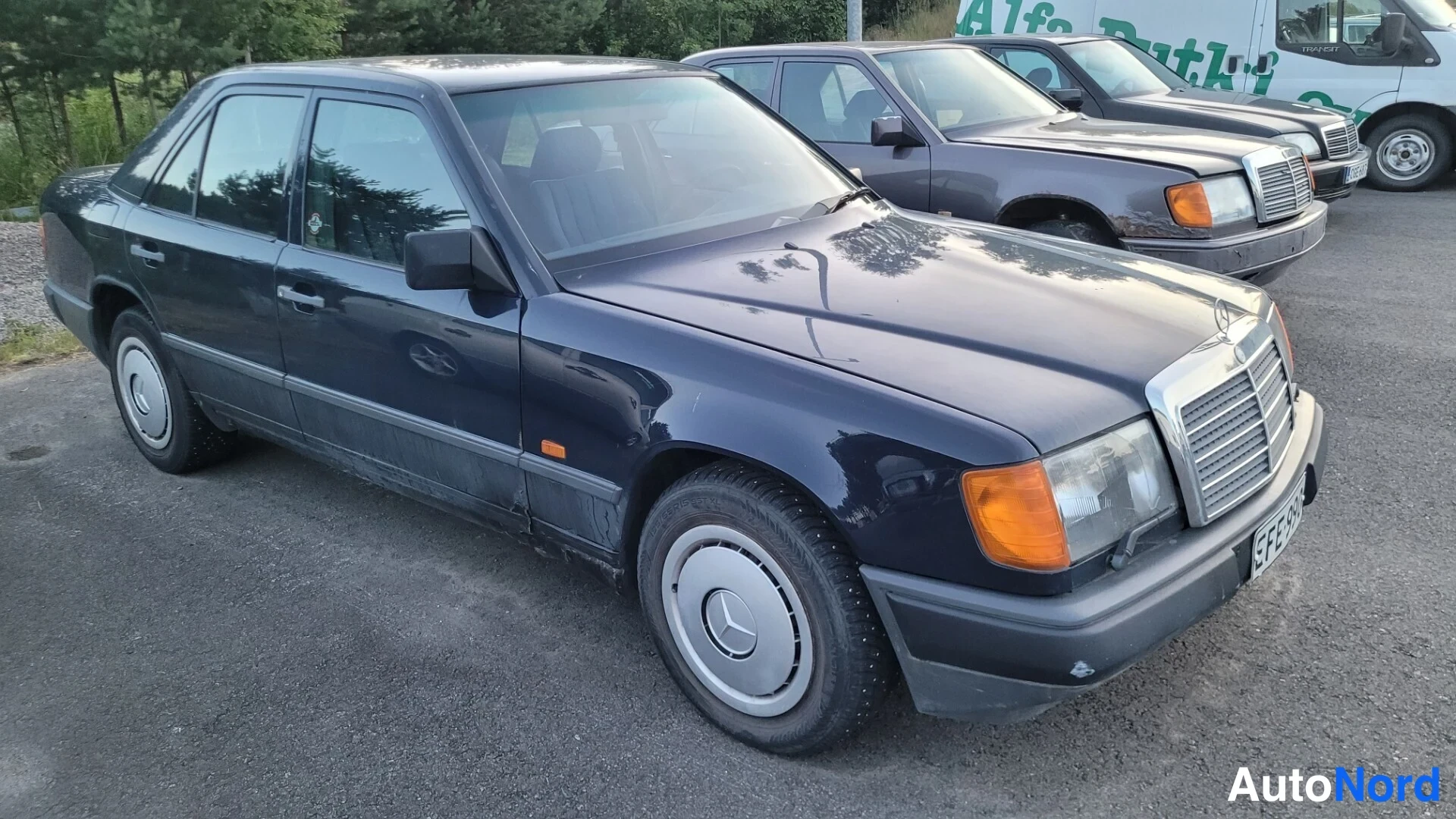 Etuviisto, nokka oikealle: Tummansininen Mercedes-Benz-sedan kolmasosa etuosasta oikealta vasemmalla etuvetoisella pyörällä näkyvä kirkas MERCEDES-merkintä etusäleikössä.