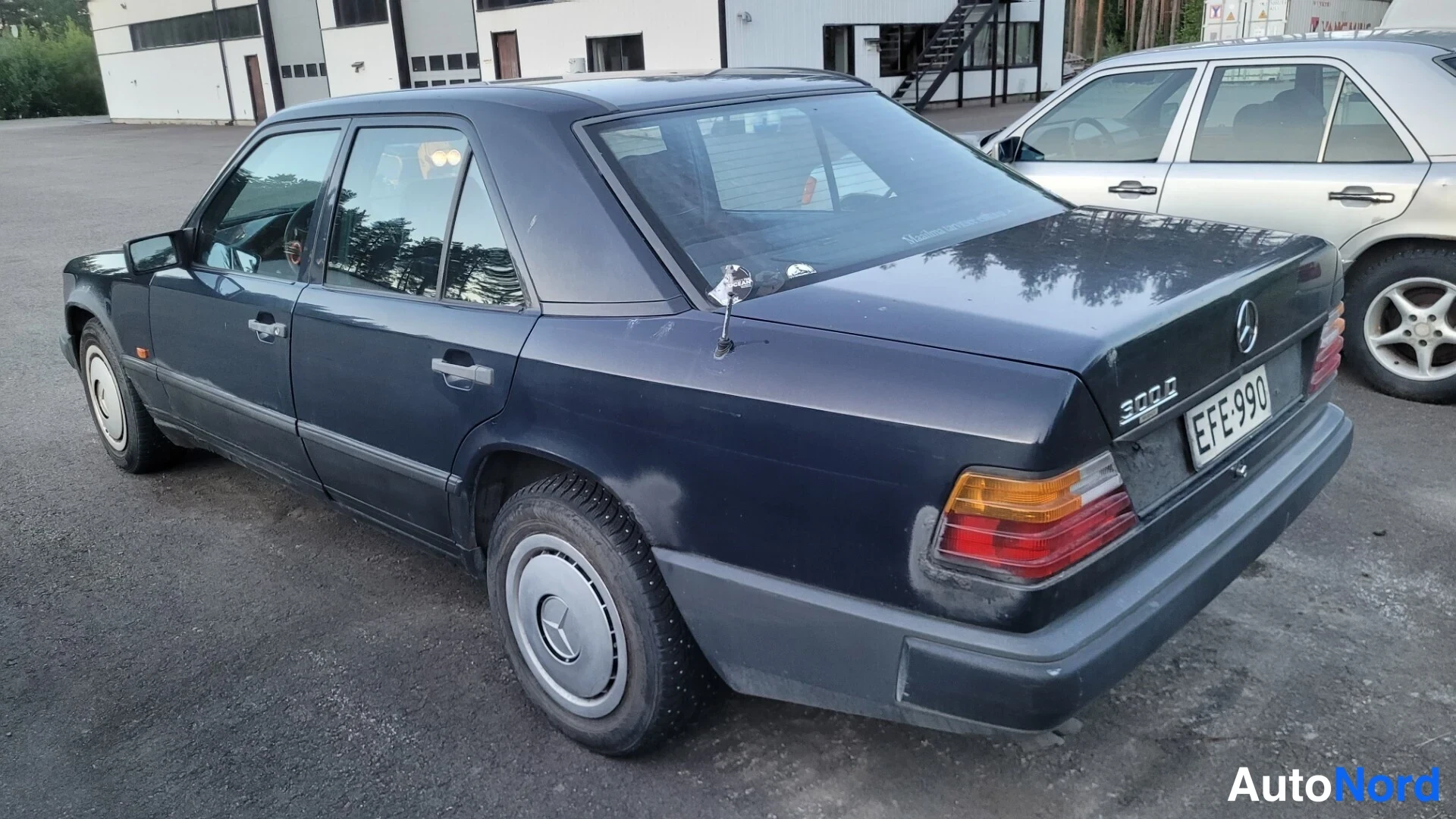 Takaviisto: Tummansininen Mercedes-Benz-sedan takapäältä oikeasta neljäsosasta, rekisteritunnus ja 300D-merkintä takaluukussa, harmaa merkintä takasuosassa.