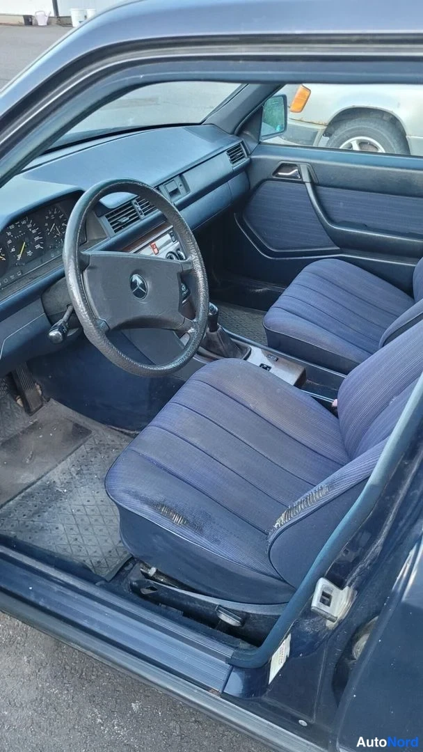 Muu: Etumatkustustila kuljettajan puolelta: Mercedes-tunnuksinen ohjauspyörä, mittaristo, manuaalivaihtoehdin vipu ja siniraitaiset penkit.