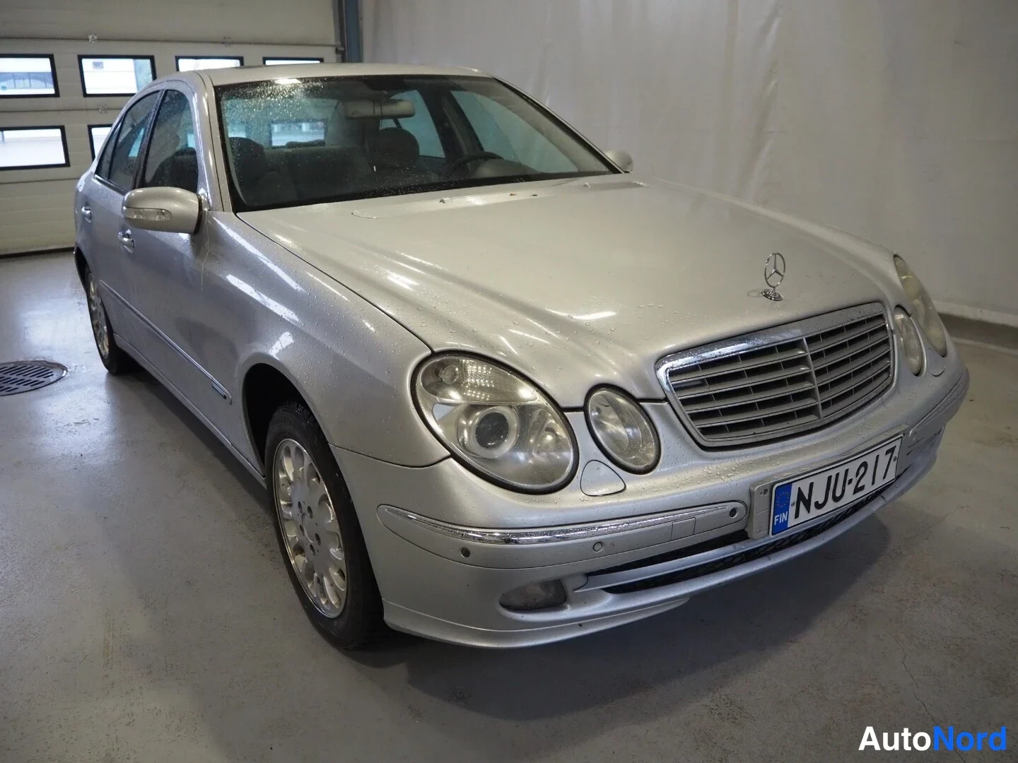 Etuviisto, nokka oikealle: Hopeinen Mercedes-Benz sedan etuviistöstä oikealta, rekisteritunnus.