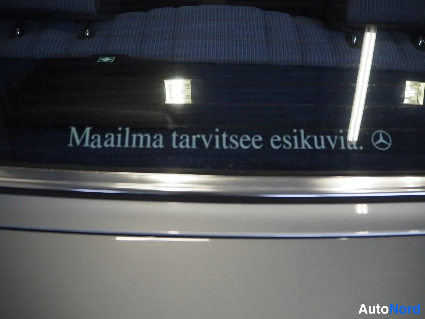 Muu: Takaistuimen selkänojan yläosaa ja koriin kaiverrettu teksti: Maailma tarvitsee esikuvia. Mercedes-tähden logolla, hopeanharmaa maali näkyvissä.