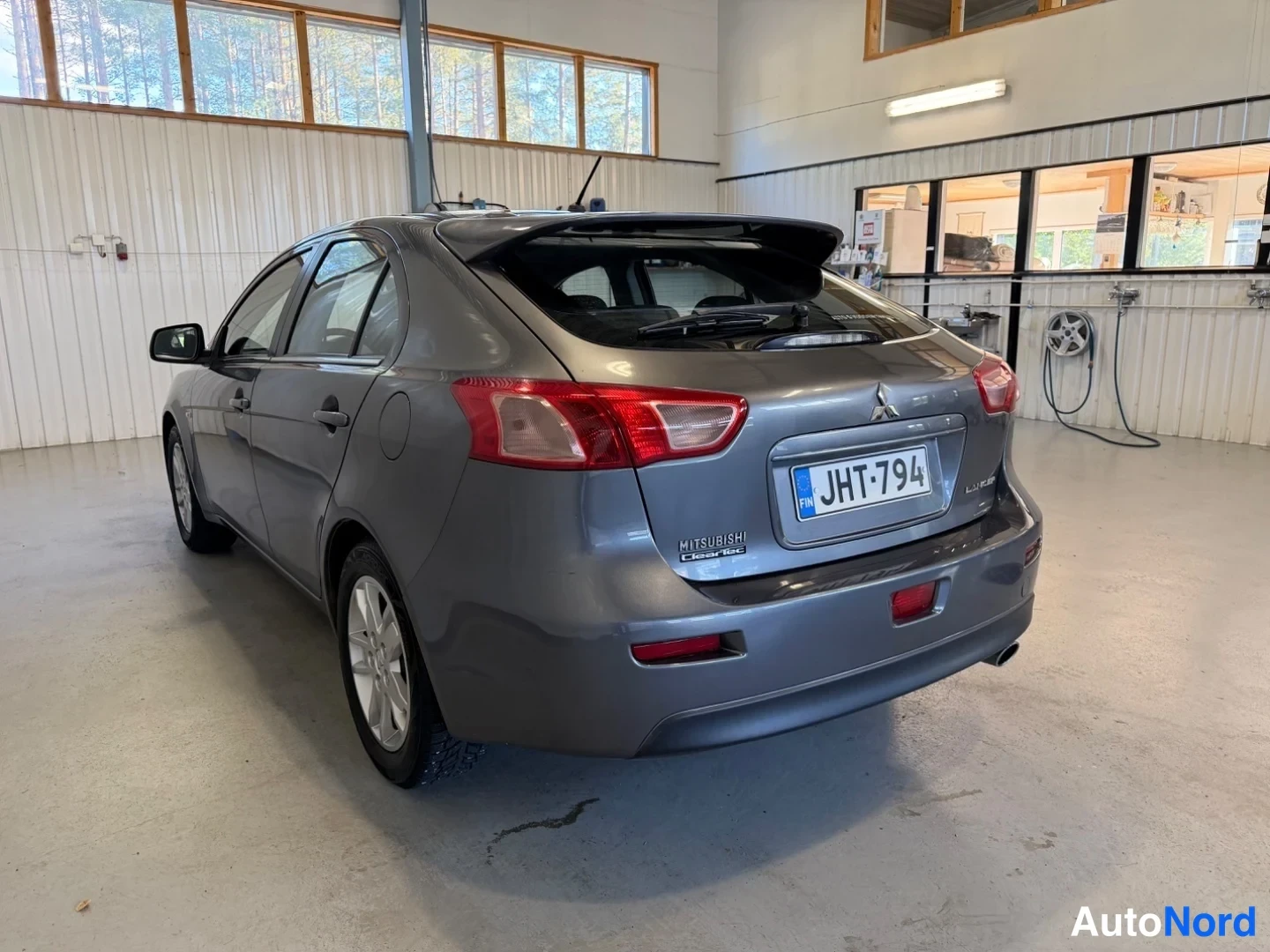 Takaviisto: Tummanharmaan Mitsubishi Lancer -auton takakulma, takapuoli ja vasen sivu näkyvät, rekisterikilpi.