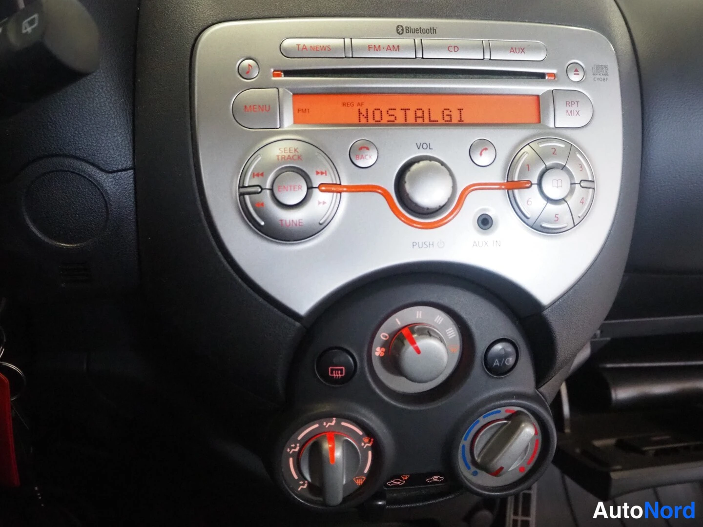 Muu: Auton radion kojelauta: Bluetooth, CD ja AUX -merkit, näytössä teksti NOSTALGI sekä A/C-painike.
