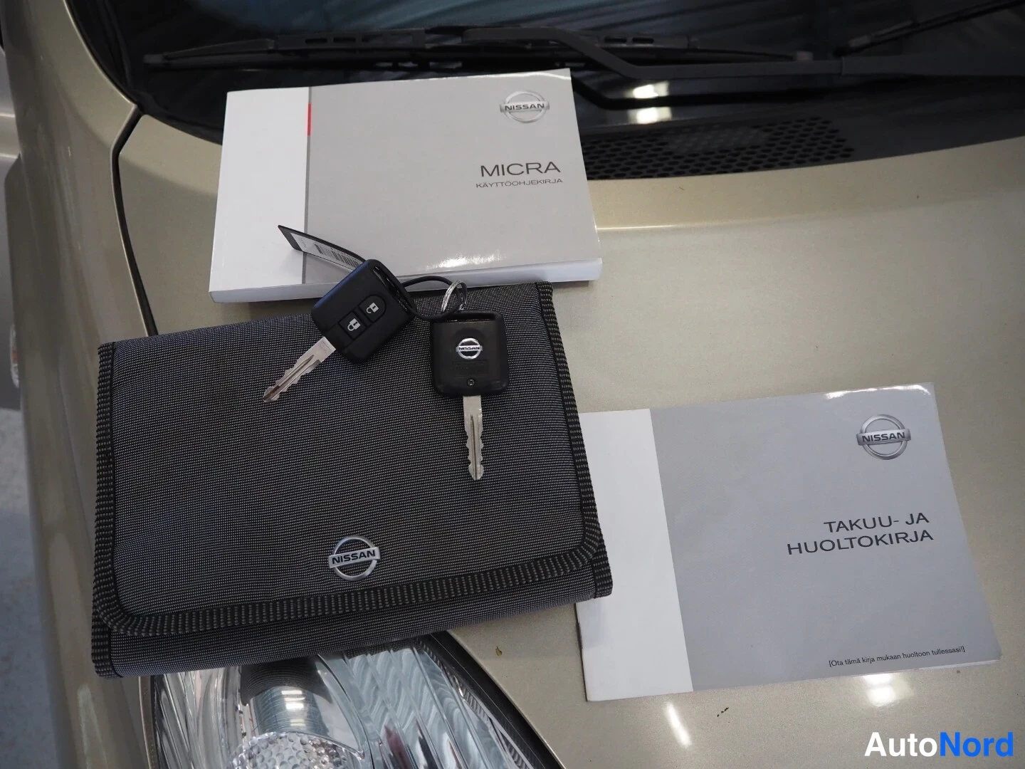 Muu: Auton konepellin päällä kaksi avainta kauko-ohjaimineen, Nissan Micra -käyttöohjekirja ja takuu- ja huoltokirja.