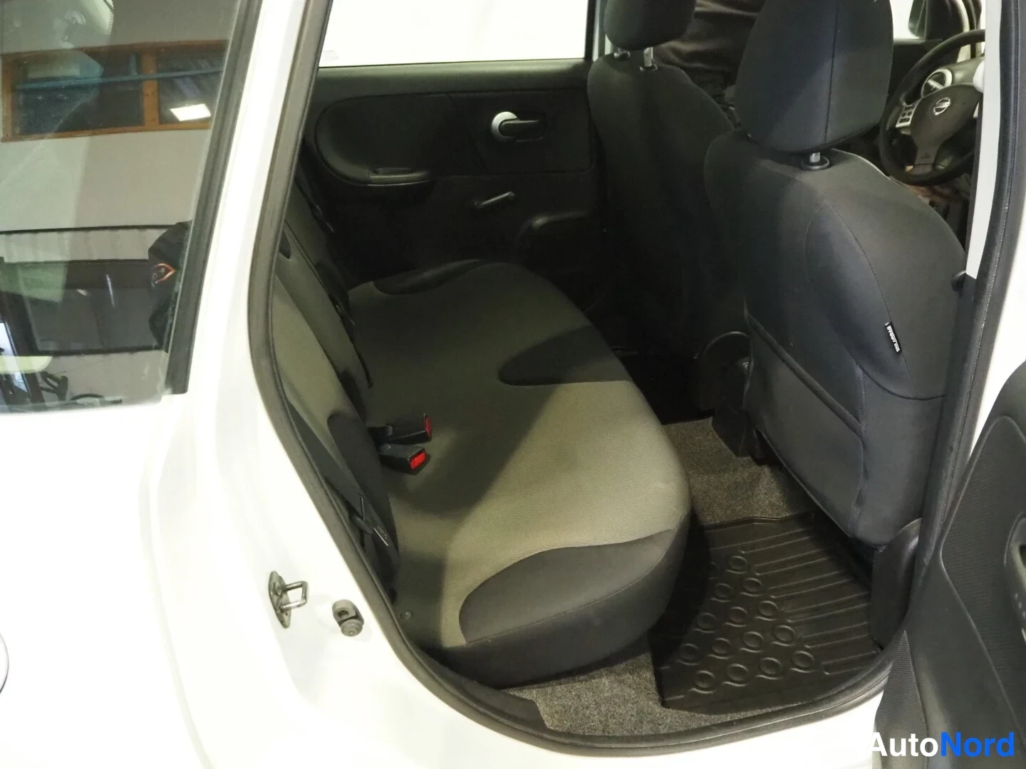 Muu: Nissan Noten takapenkin näkymä avatusta ovesta, tummat penkit ja kumimatot lattiassa.