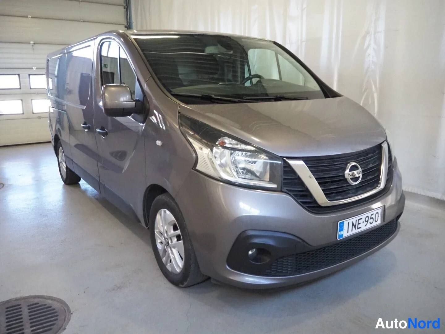 Etuviisto, nokka oikealle: Harmaanruskea Nissan NV300 -pakettiauto kuvattu kolmivirstapisteestä edestä oikealta, rekisterikilpi näkyvissä.