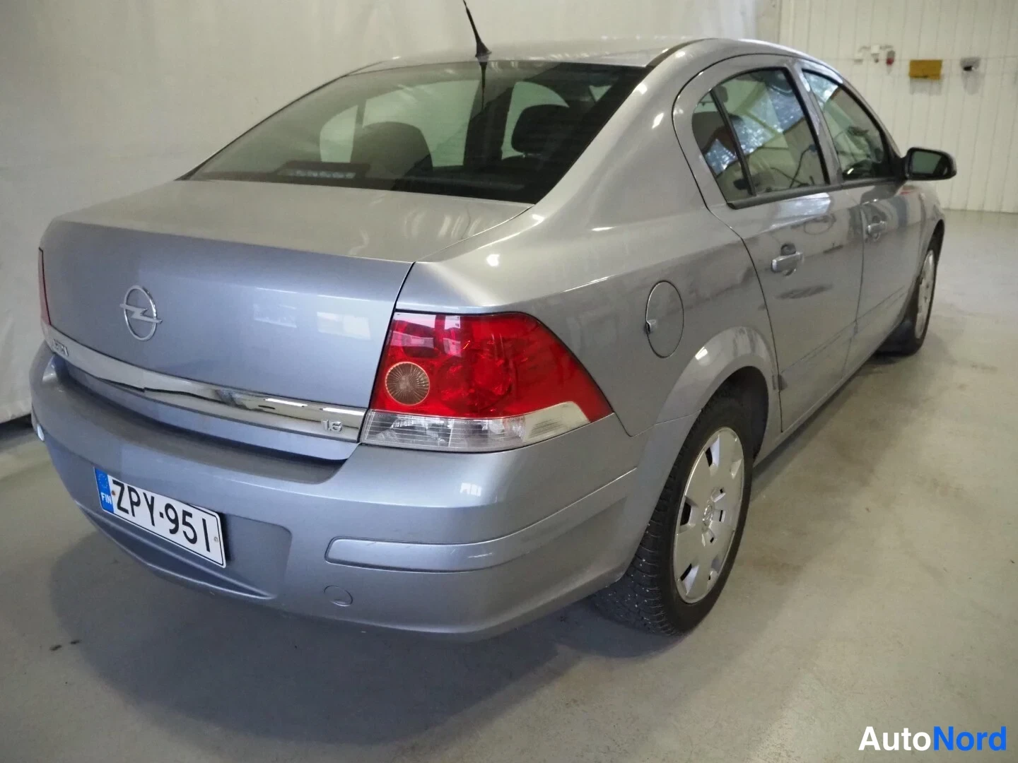Takaviisto: Hopeanharmaa Opel Astra -sedan takaosa ja oikea kylki takaa oikealta kuvattuna, rekisteritunnus.