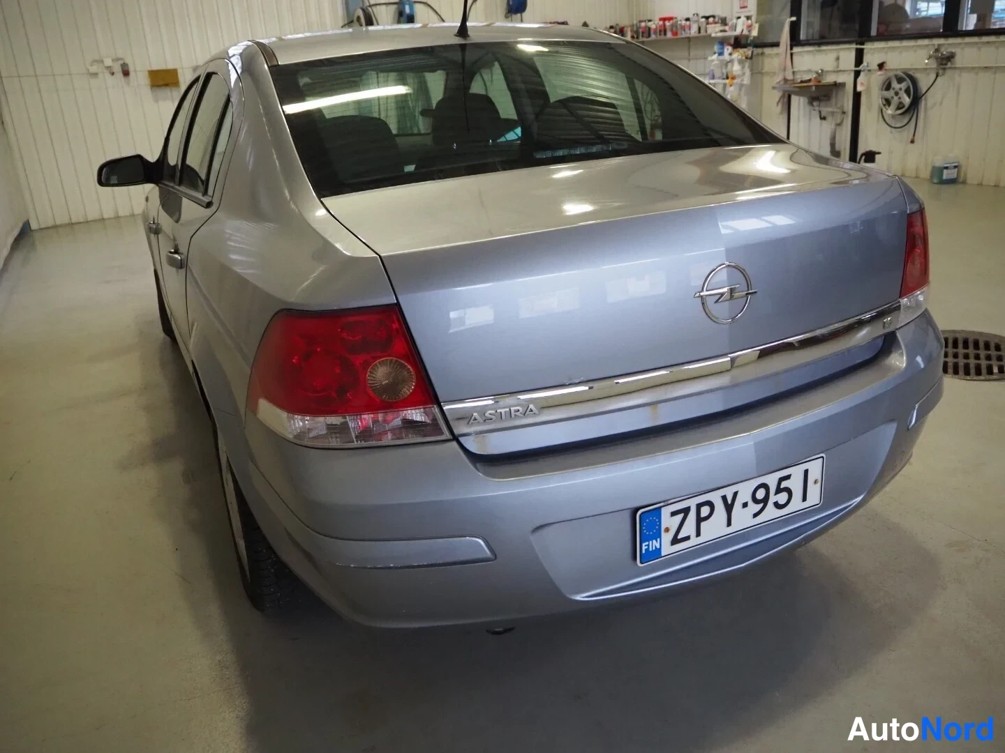 Takaviisto: Hopeanharmaa Opel Astra -sedan takaosa ja vasen kylki takaa vasemmalta kuvattuna, Astra-teksti takaluukussa, rekisteritunnus.
