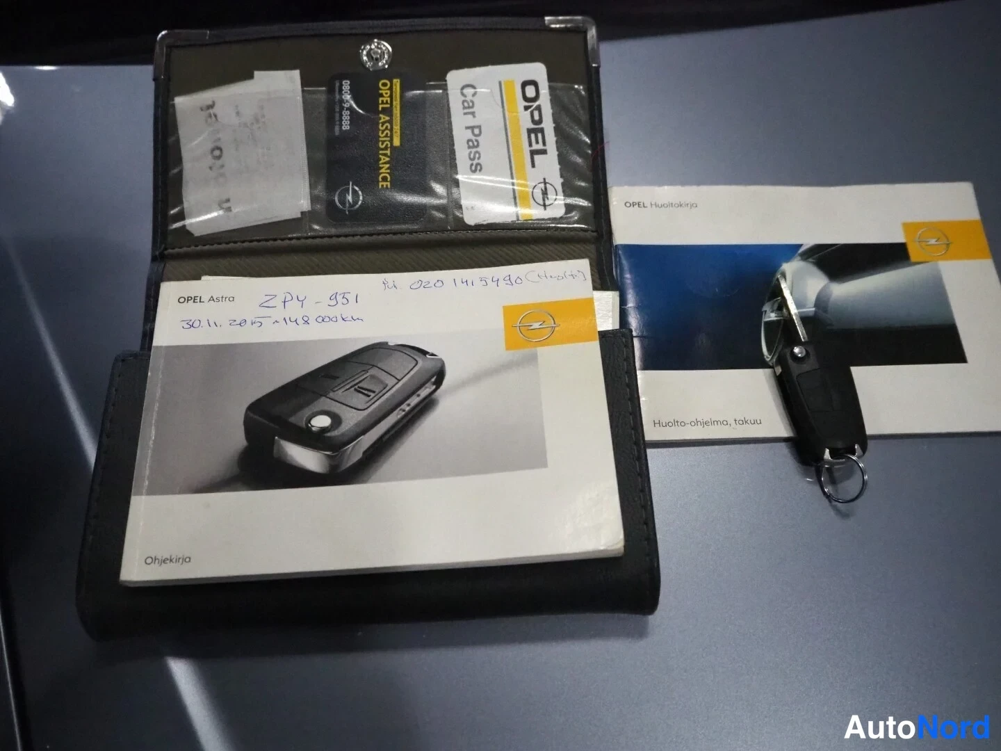 Muu: Opel Astra -kansiokansio avattuna, sisällä Opel Car Pass -kortti ja Opel Assistance -kortti, vieressä avain ja Opel Huoltokirja -esite.