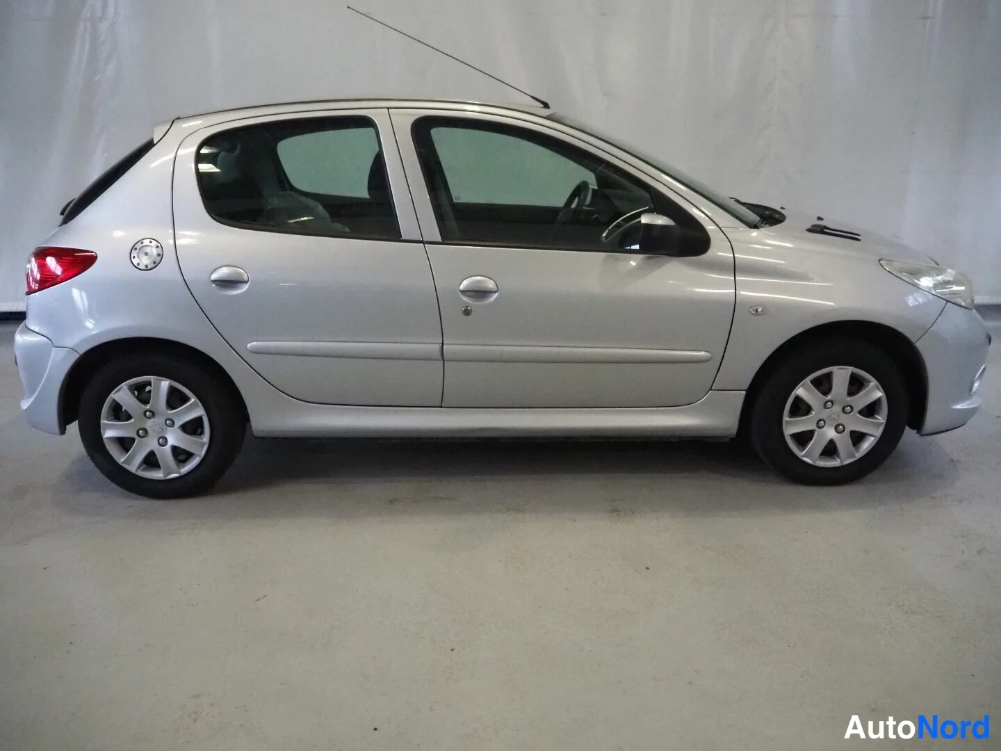 Etuviisto, nokka oikealle: Hopeanvärinen viisiovinen Peugeot 206+ -henkilöauto sivulta oikealta sisätilassa.