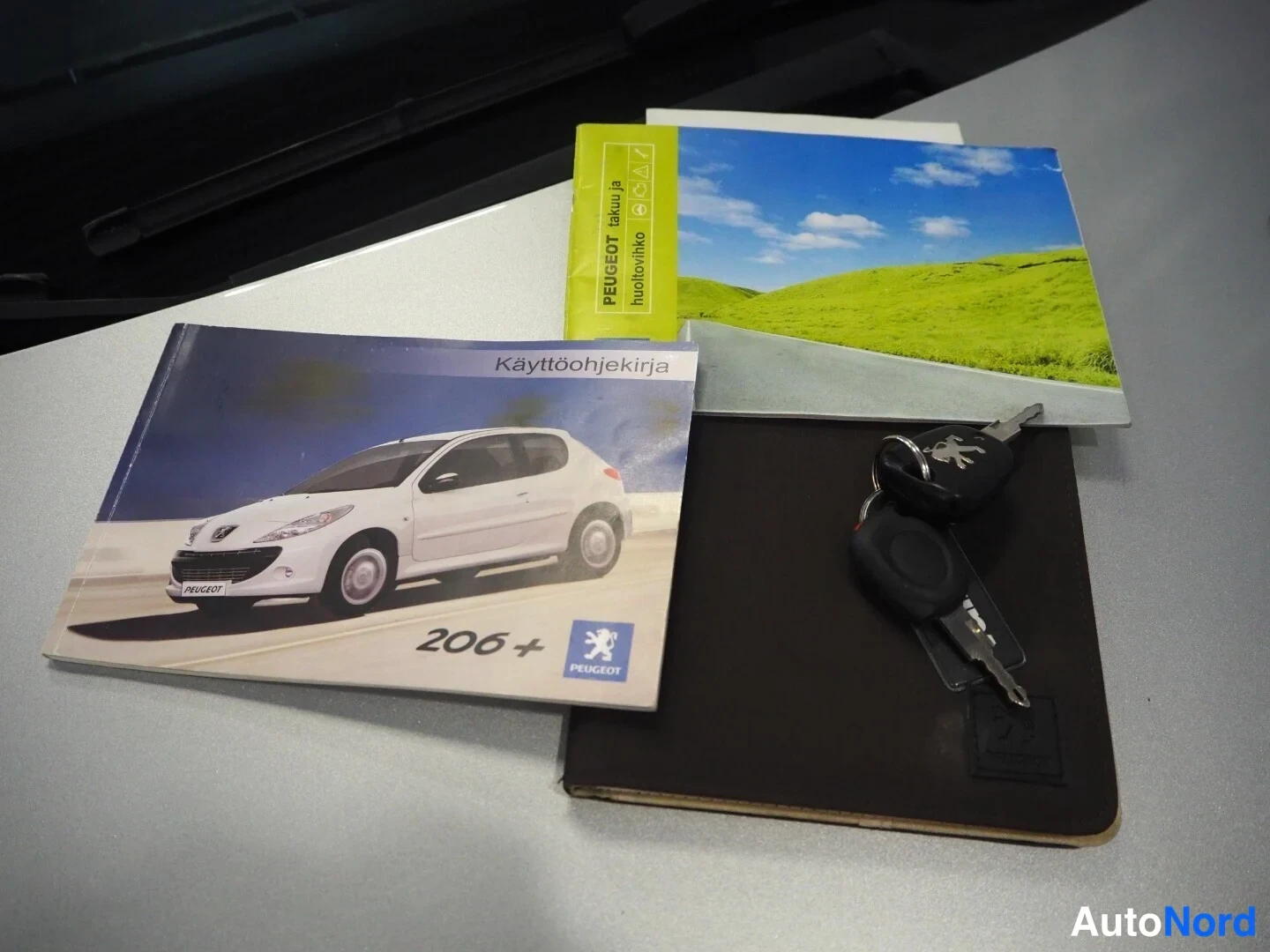 Yksityiskohta: Peugeot 206+ -kayttöohjekirja, huoltokirja ja kaksi avainnipussa auton päällä.
