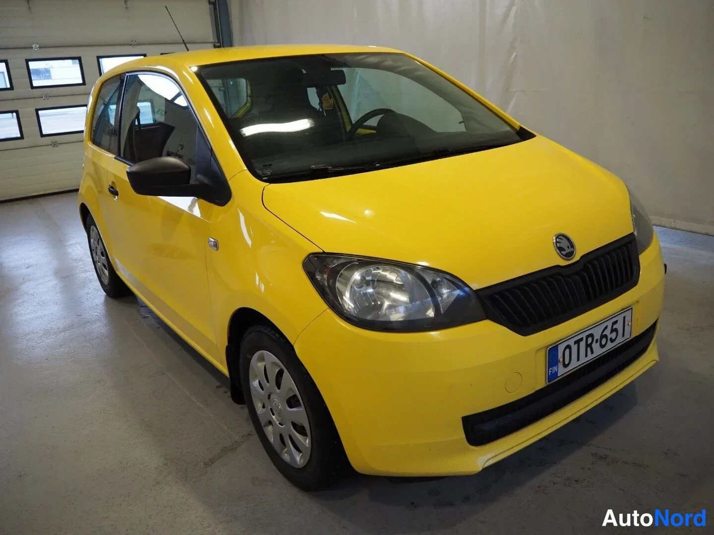 Etuviisto, nokka oikealle: Keltainen Skoda Citigo -henkilöauto kulmassa kuvattuna etupää ja oikea kylki näkyvissä, rekisterikilpi.