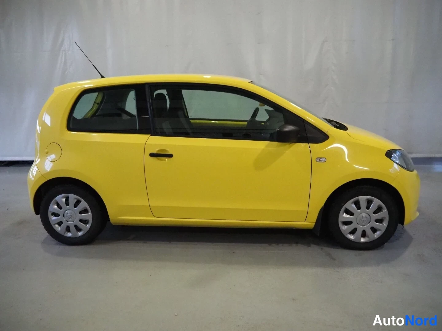 Sivulta: Keltaisen Skoda Citigo -henkilöauton sivukuva oikealta kyljeltä sisätiloissa.