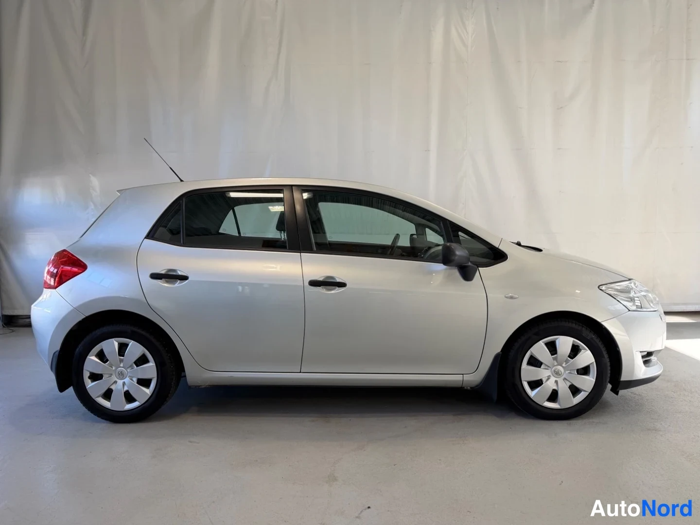 Sivulta: Hopeanvärinen Toyota Auris sivulta oikealta, viisiovinen viistoperä, hallitilassa.