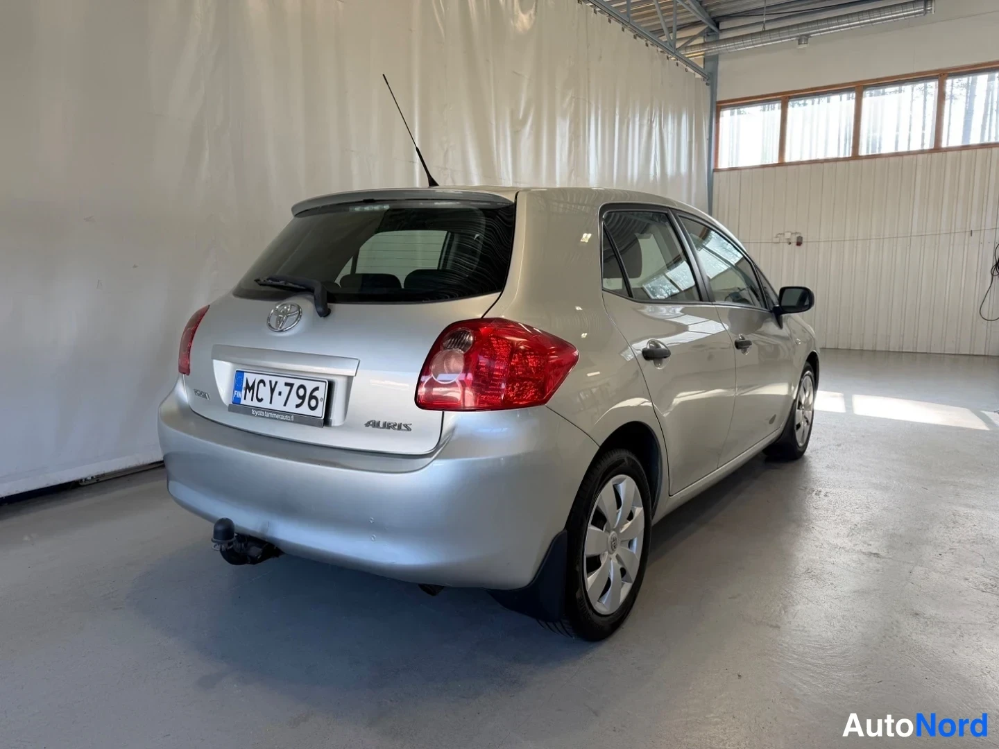 Takaviisto: Hopeanvärinen Toyota Auris takaa kolmannesvälikulmasta vasemmalle, rekisterikilpi, hallitila.