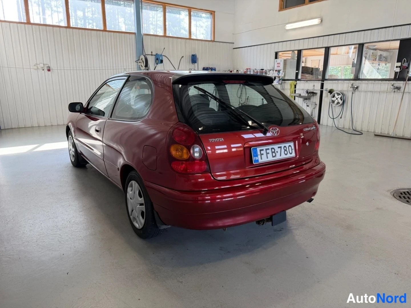 Takaviisto: Punaisen Toyota Corolla -viistoperän takakolmannes autotallin sisällä, rekisterikilpi.